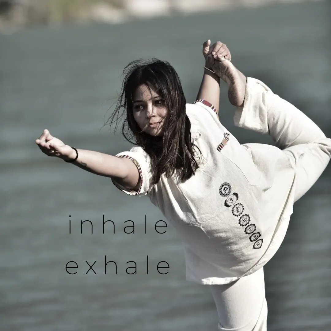 Anupriya in a standing dancer pose by the water, with the words inhale and exhale beside her