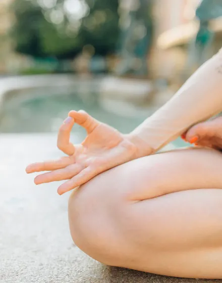 A hand resting in a gyan mudra on a crossed knee, with a soft green garden behind