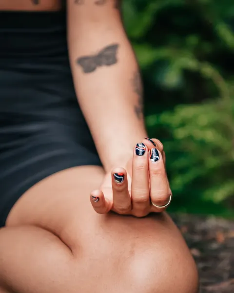 An arm and hand resting on a bent knee, with soft green foliage out of focus behind