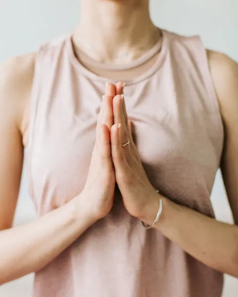 A woman in a pale pink top pressing her palms together at her chest in a prayer position